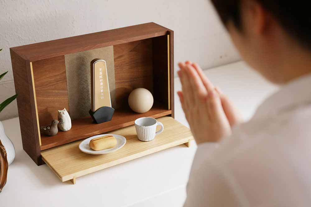 お仏壇「GAKU」の桐（生成）に手を合わせる様子